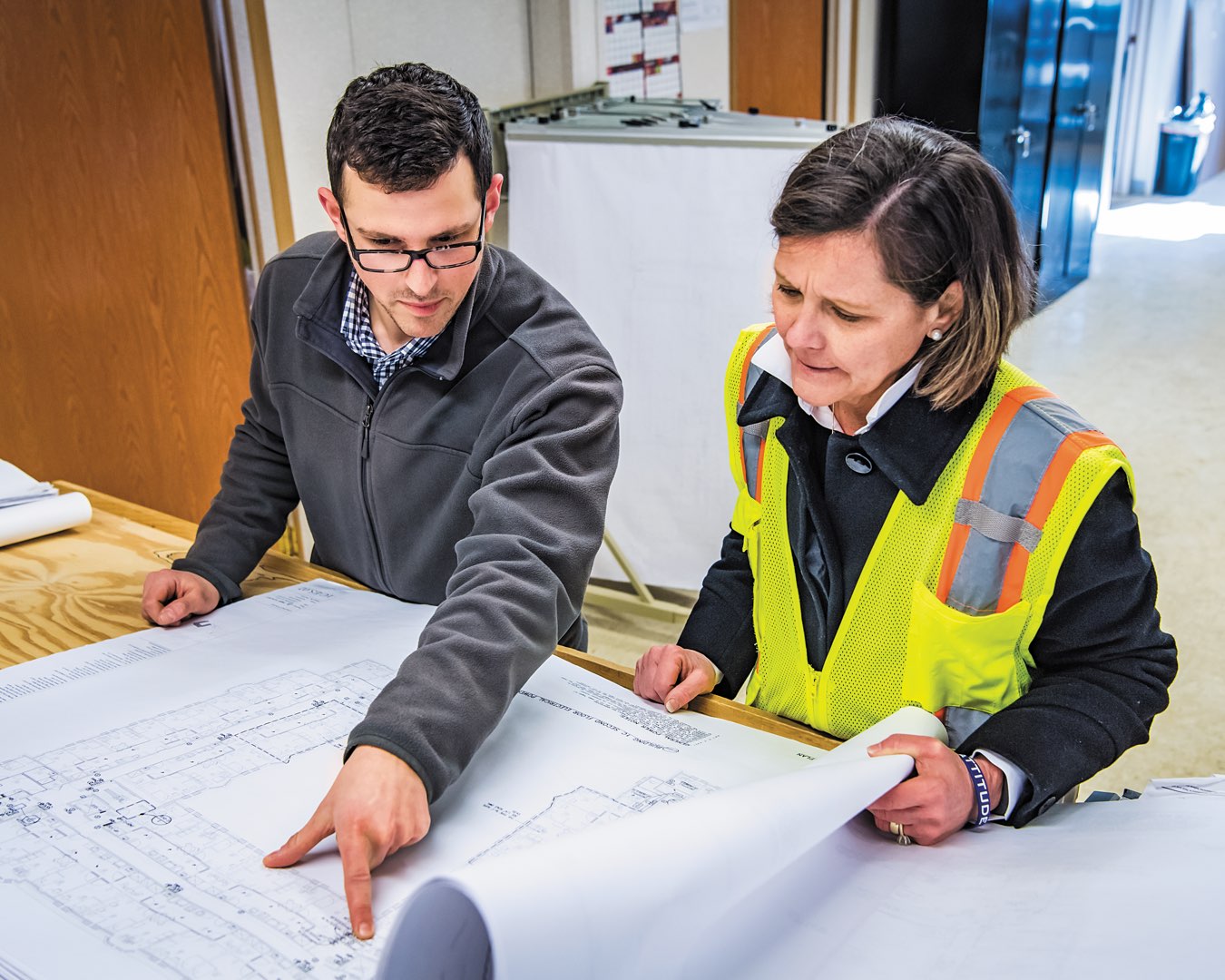 Torcon project engineer points to a detail on architectural plans he’s discussing with Marilou Smith standing beside him