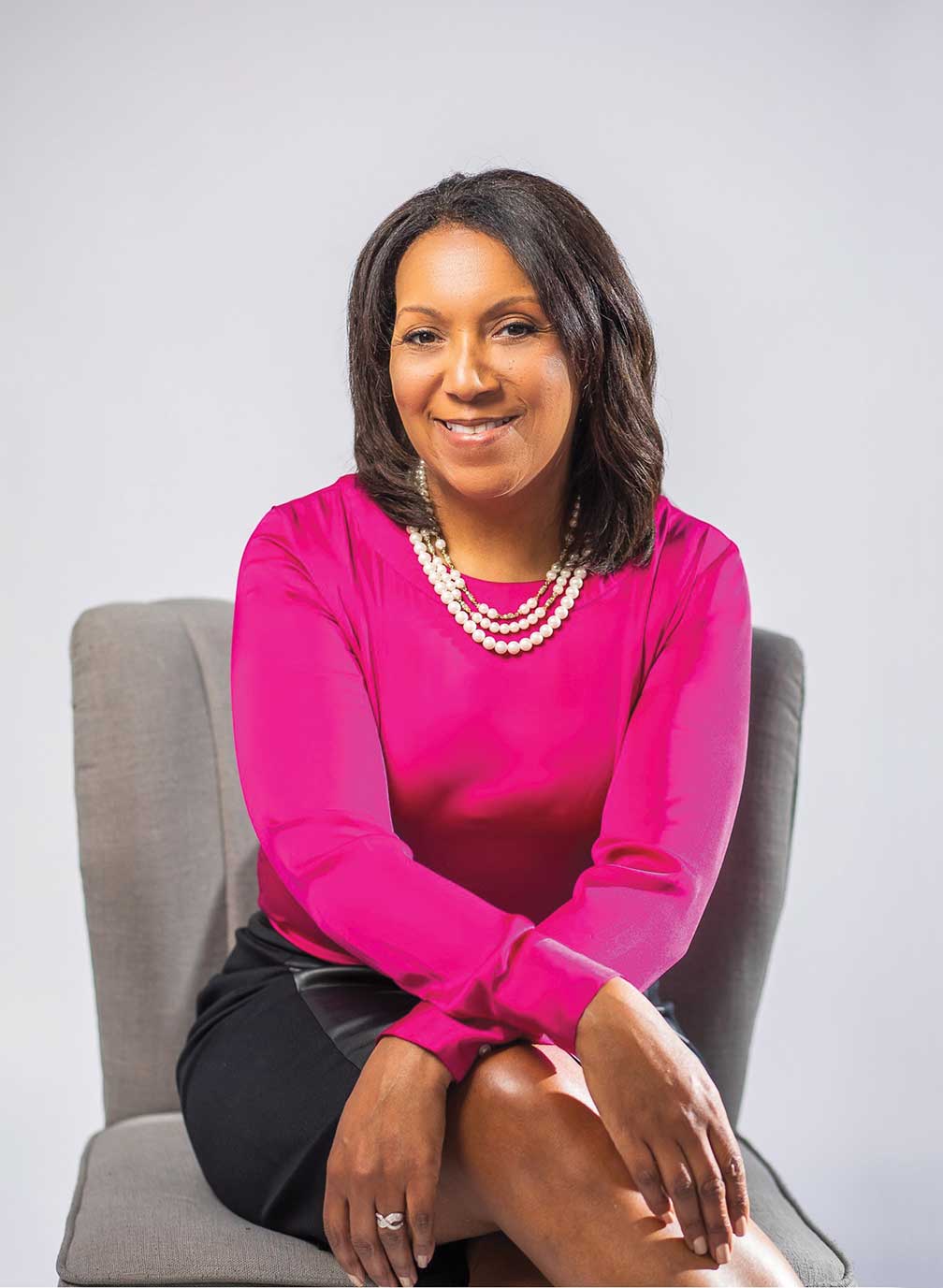 Kimberly Kersey sitting on a desk chair in a bright pink sweater