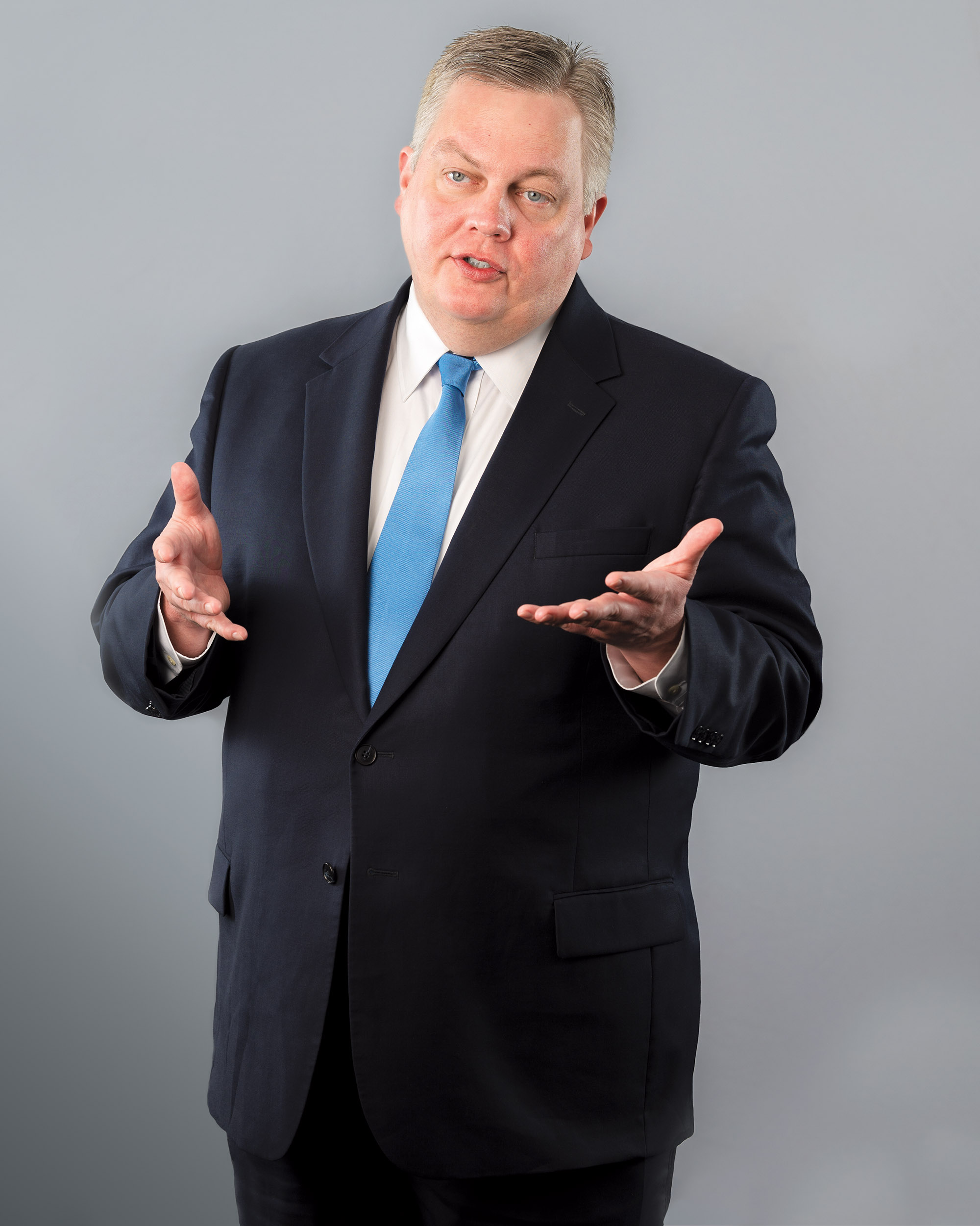 Mike Moreland talking with his hands in a navy suit jacket and blue tie