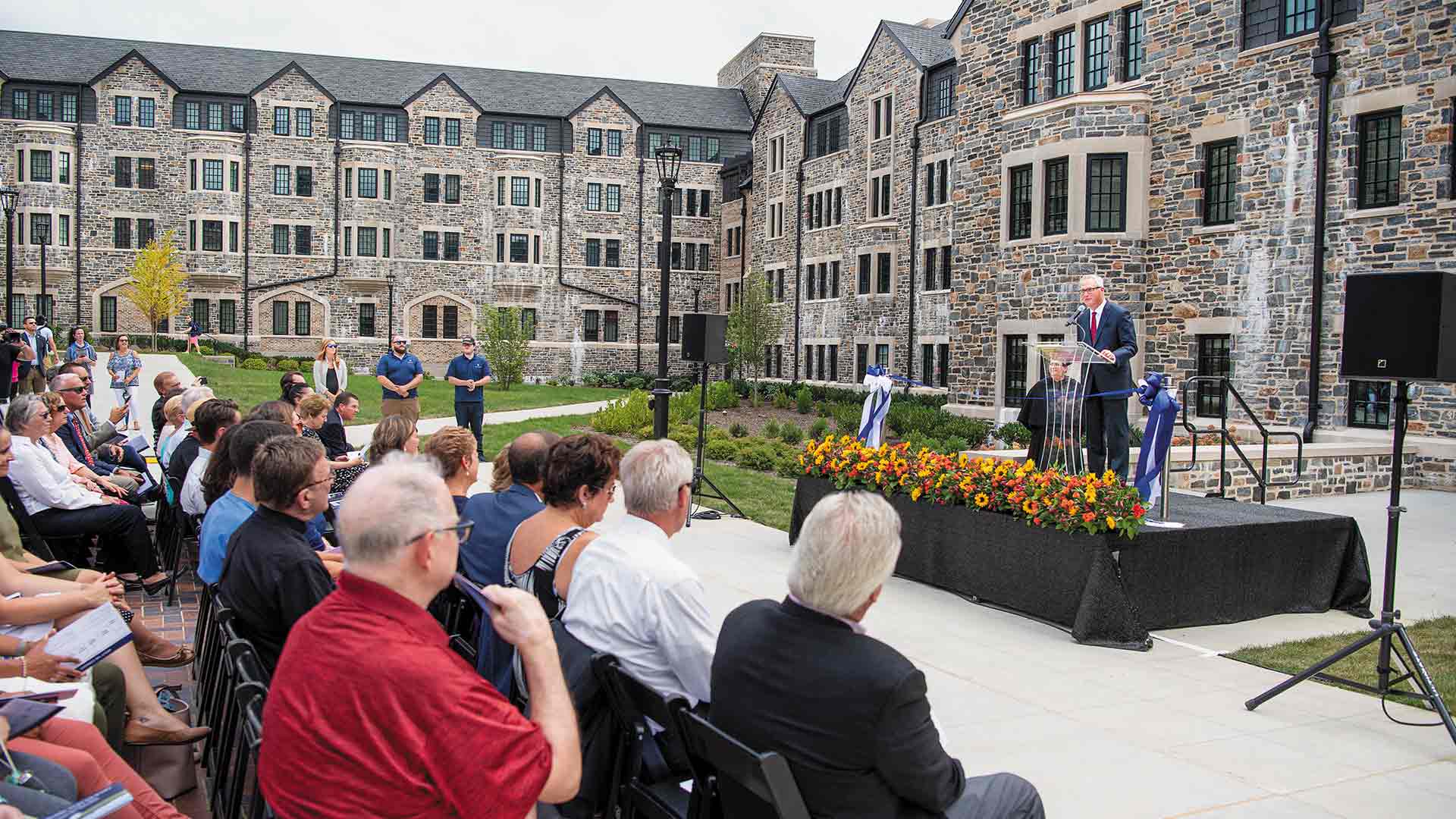 Ken Valosky on stage speaking from behind a podium before a crowd at The Commons opening ceremony