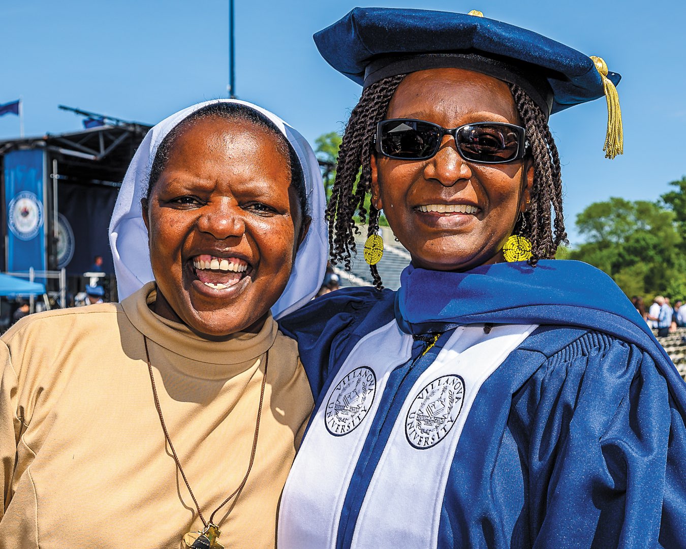 Sister Jackline Mayaka wearing her religious habit and white veil with faculty member in graduation regalia