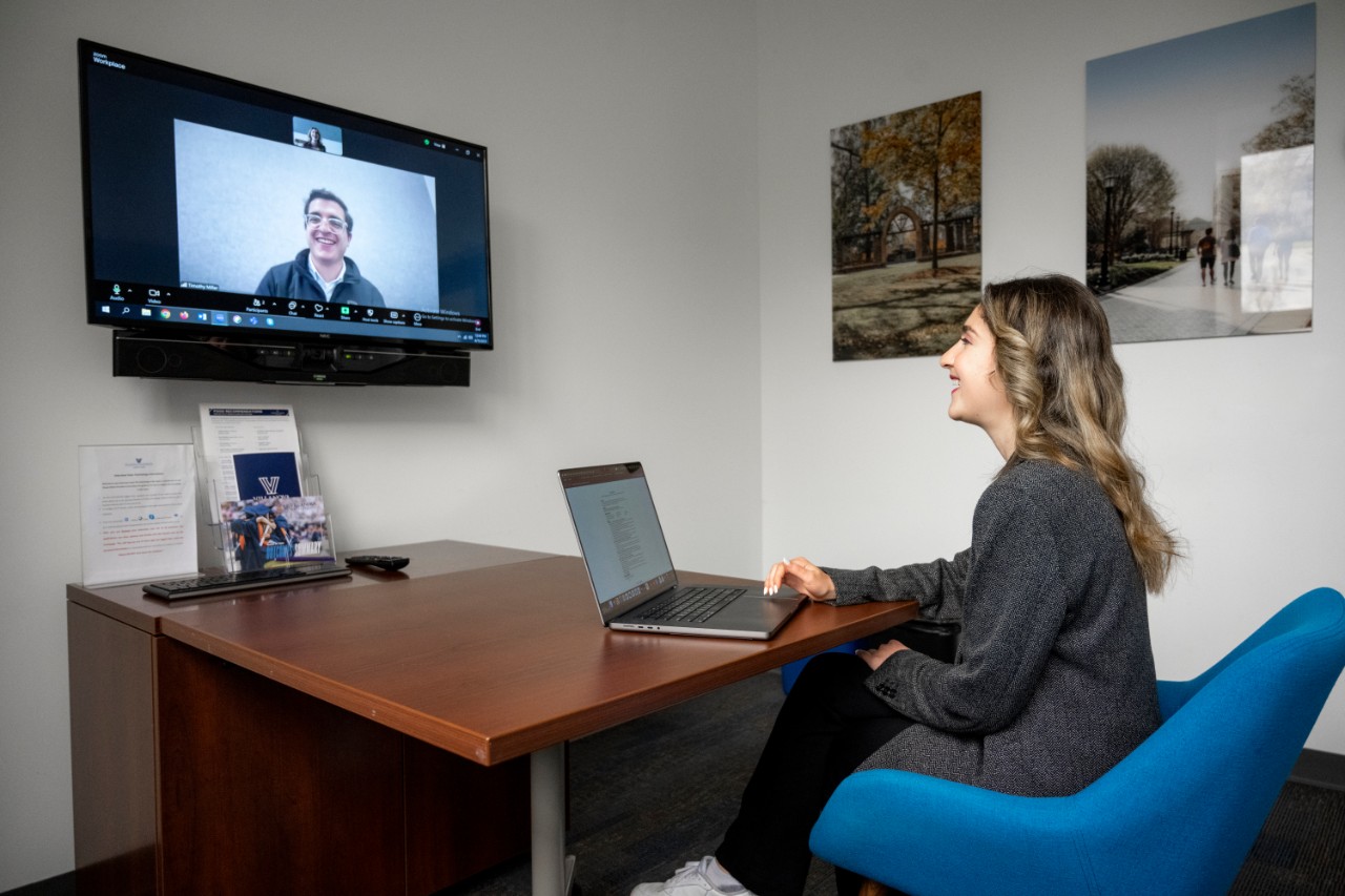Student sitting in chair being interviewed by an employer on a screen in front of the student.