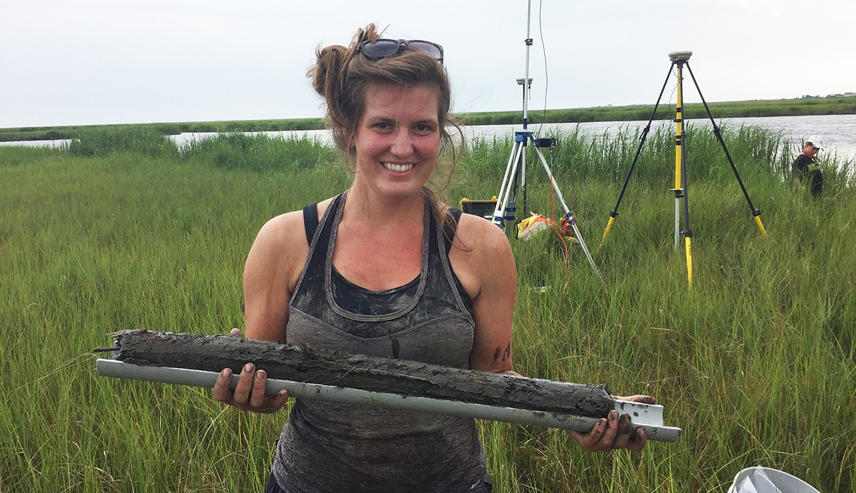 Environmental Science graduate student holding a soil core from a tidal wetlands area.