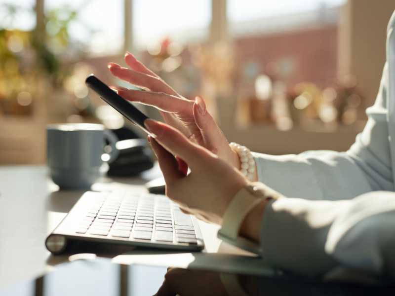 person holding and swiping on a smartphone with a laptop keyboard in the background