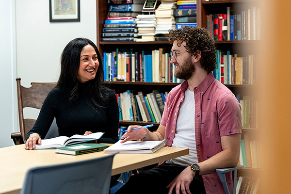 Philosophy professor and PhD student sitting at a table in front of bookshelves