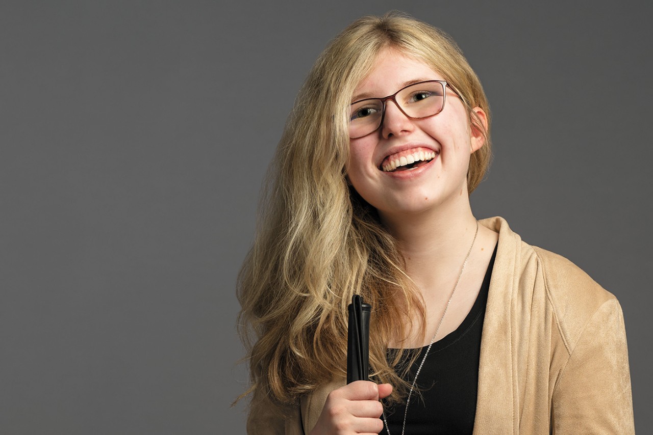 student Kaleigh Brendle, who is visually impaired, smiles and stands holding her cane
