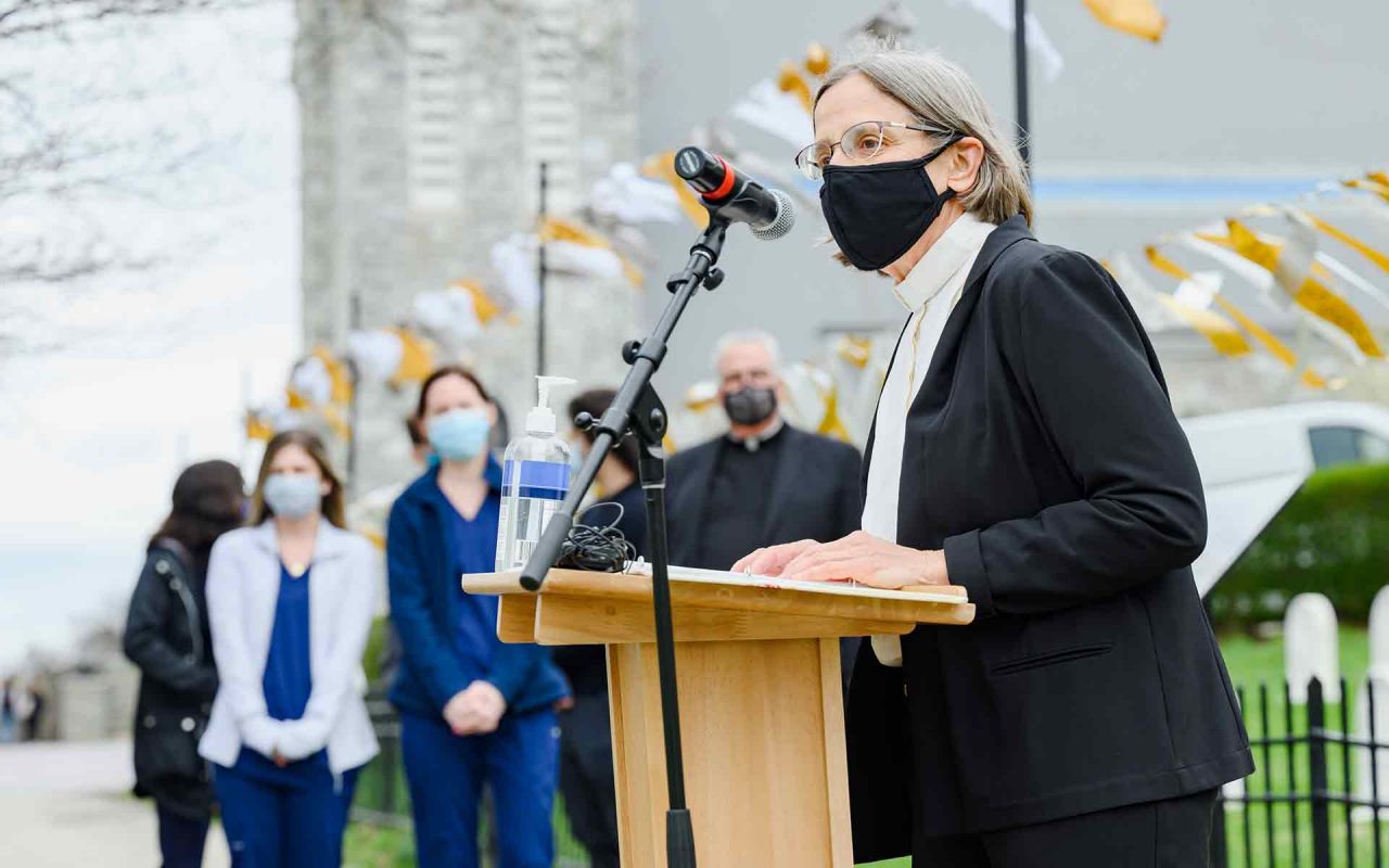 a woman speaks at a podium during the opening vigil for the COVID Memorial